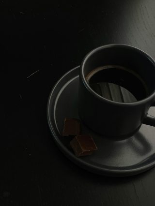 A cup of coffee on a saucer with a piece of chocolate
